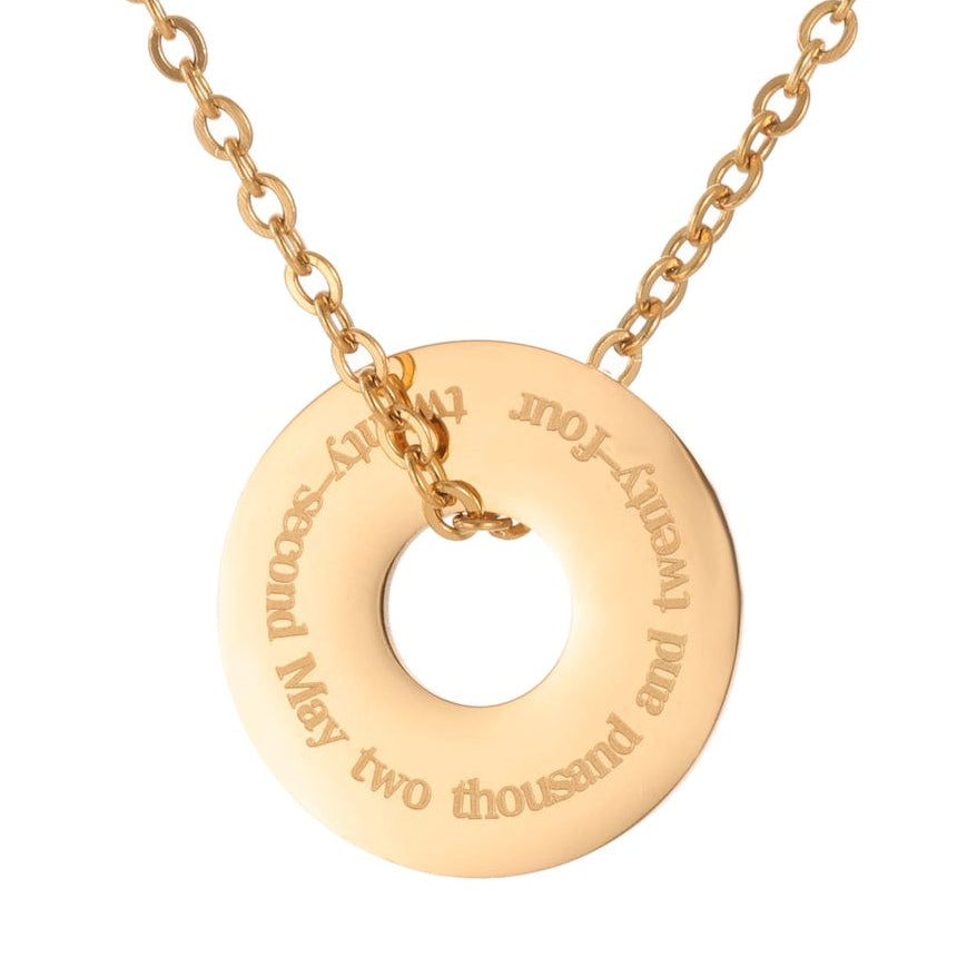 Gold necklace with a round pendant on a white background engraved with a date in full text