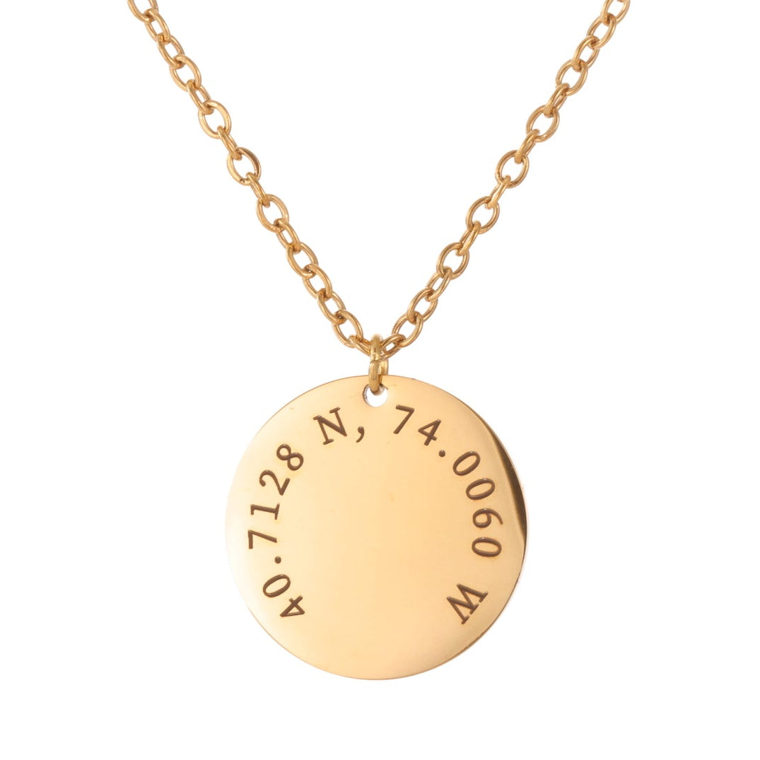 Gold necklace with a round pendant displaying coordinates on a white background