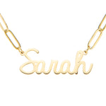 A gold-plated personalized name necklace with the name 'Sarah' written in a cursive script font, attached to a paperclip chain.
